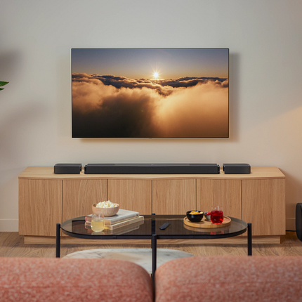 JBL Bar 1300MK2 pe o comodă TV, cu subwooferul alături, într-o cameră de zi