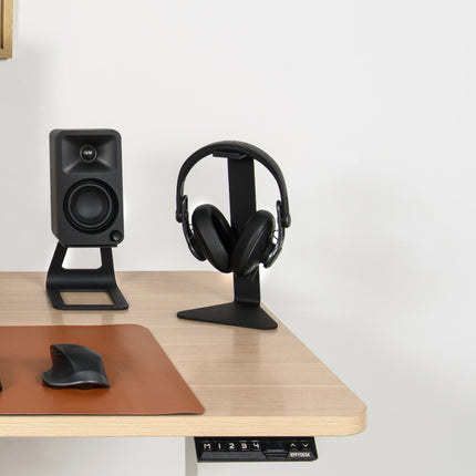 Suport Kanto Audio H1 negru, cu căști, pe un birou din lemn lângă o boxă Kanto