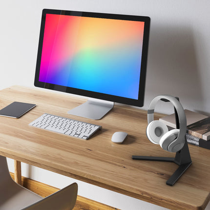 Suport Kanto Audio H3 negru, cu căști albe, pe un birou din lemn lângă un monitor