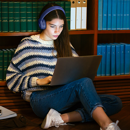 Căști JBL Tune 680NC albastre, purtate la lucru pe laptop, într-o bibliotecă