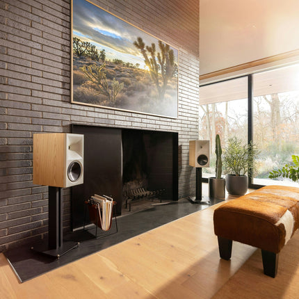 Pereche Klipsch The Nines II in finisaj Oak, cu grilele scoase, pe stative langa un semineu