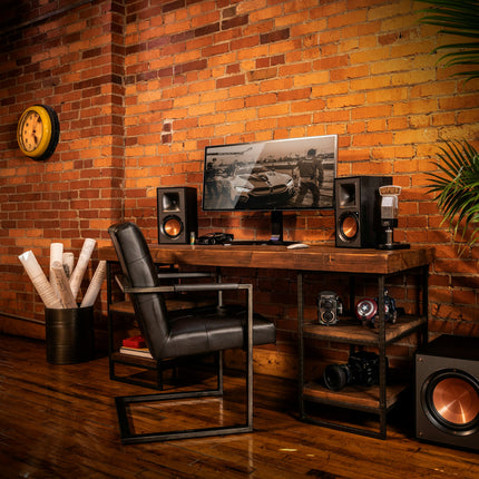 Klipsch R-51PM de o parte si de alta a unui monitor, pe un birou de lemn