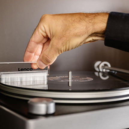 O mână trece o perie peste un disc de vinil așezat pe platanul Lenco L-455