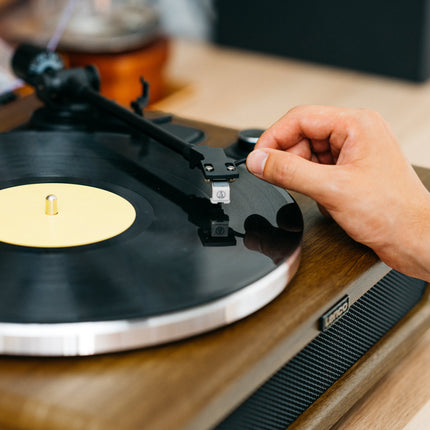 O mână coboară brațul Lenco LS-410 cu doza Audio-Technica pe un disc de vinil