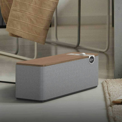 Boxa Klipsch The One Plus in finisaj Walnut, asezata pe pardoseala langa un fotoliu