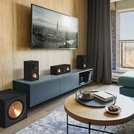 Perechea Klipsch R-50M fara grile, la capetele unei comode sub televizor, alaturi de un canal central si un subwoofer