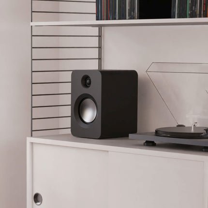 Boxă Kanto Audio REN neagră pe o etajeră, lângă un pick-up