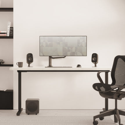 Pereche Kanto Audio UKI Black pe un birou, cu un subwoofer dedesubt