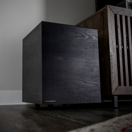 Subwooferul wireless al sistemului Klipsch Cinema 600, asezat pe podea langa o comoda