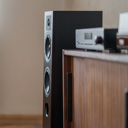 Indiana Line Diva 5 neagră, lângă o comodă din lemn cu un amplificator