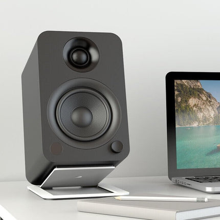 Boxă Kanto Audio YU neagră pe un stand de birou, lângă un laptop