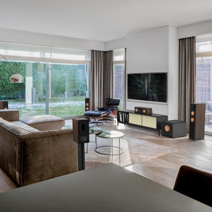 Living cu ferestre mari și un sistem Klipsch Reference Premiere, cu subwooferul lângă comodă