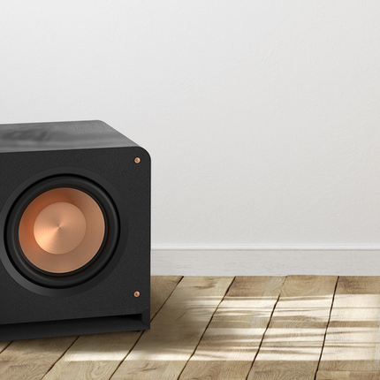 Klipsch RP-1200SW pe o pardoseală de lemn, lângă o plantă