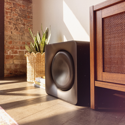 Klipsch Flexus SUB 200 asezat pe podea intr-un living, langa o comoda de lemn