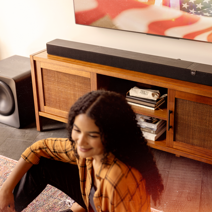 Klipsch Flexus SUB 200 pe podea, langa un soundbar Flexus Core 300 asezat sub televizor