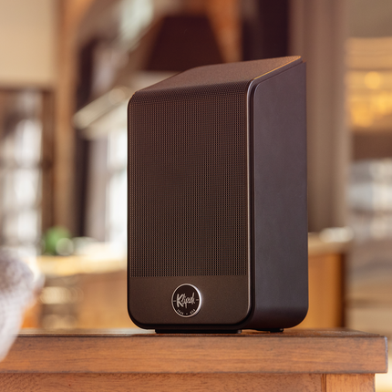 Prim-plan cu o boxa Klipsch Flexus SURR 200 asezata pe o masa de lemn intr-un interior luminos