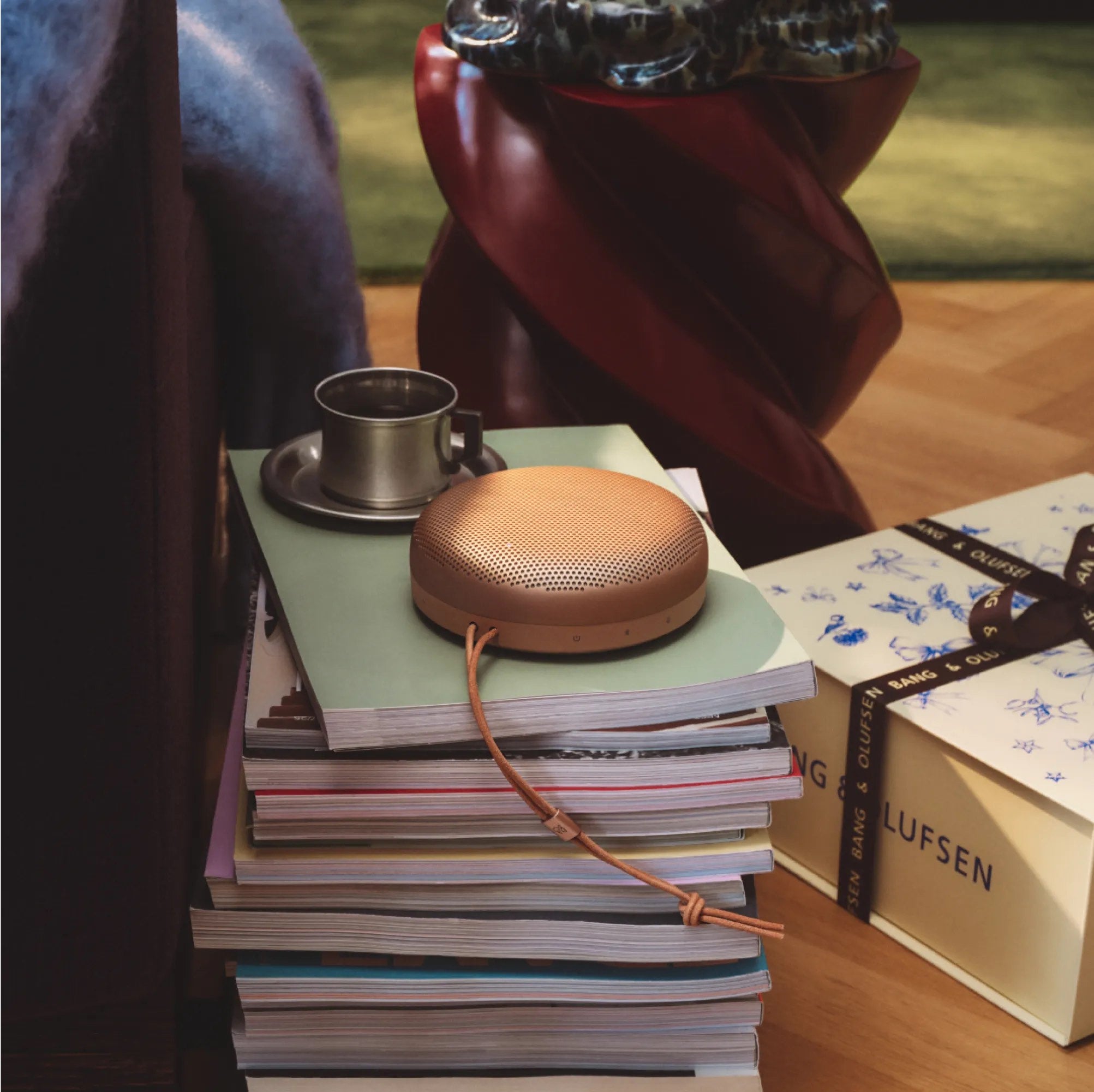 Beosound A1 în finisaj Honey Tone, așezată pe un teanc de reviste și cataloage Bang & Olufsen.